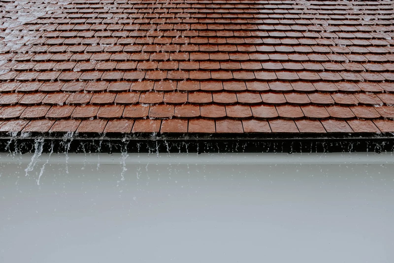 Regenwater stroomt over een pannendak en de dakrand